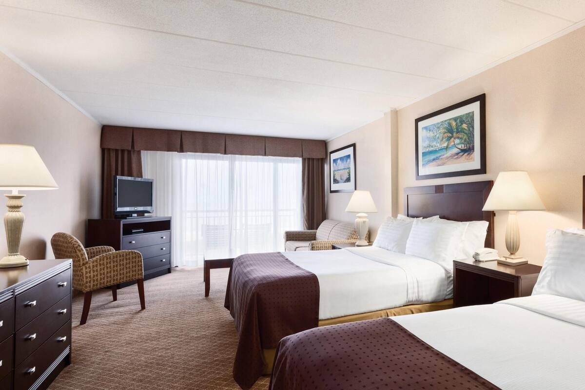 A hotel room with two beds, a desk, a TV, and a chair.
