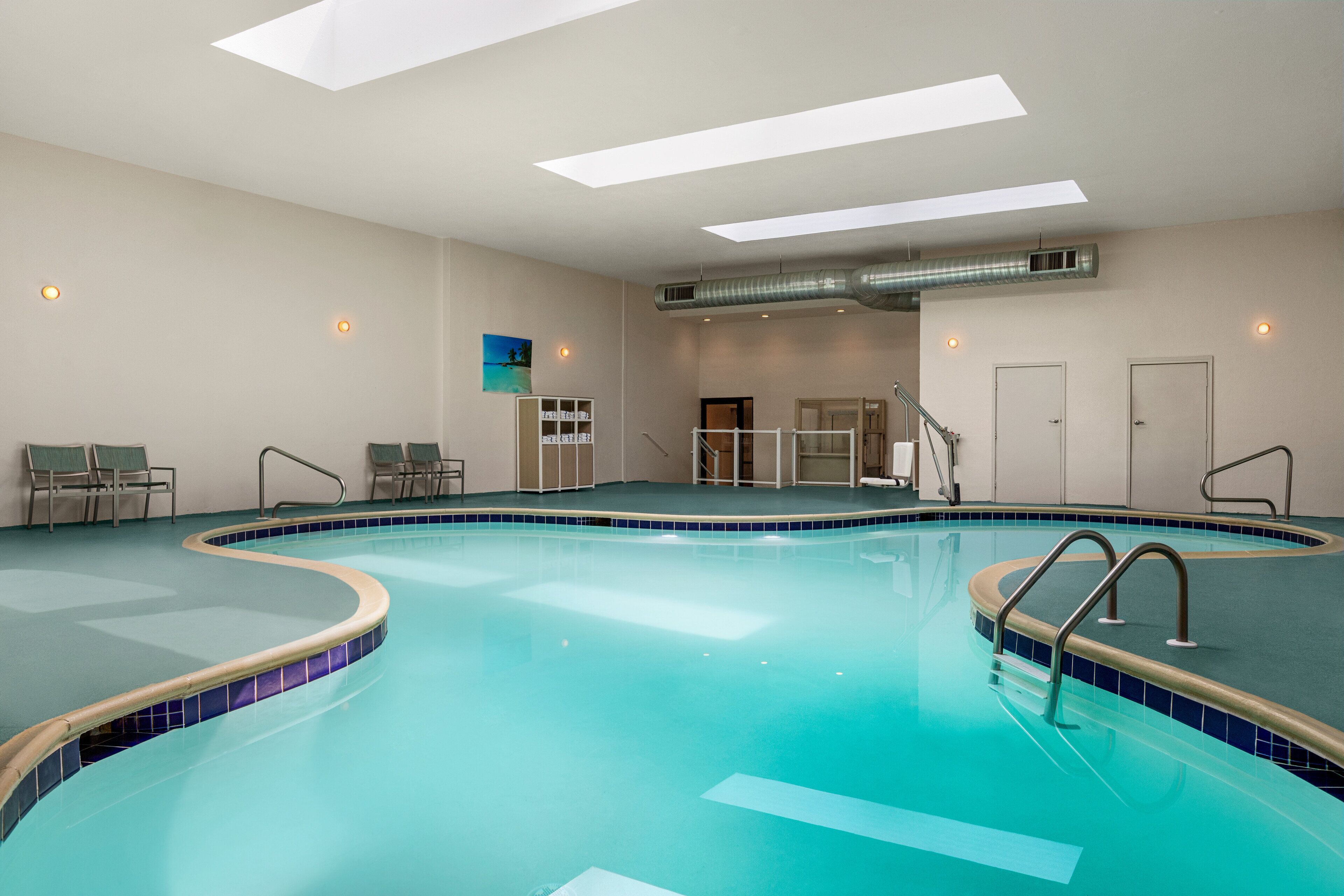 An indoor swimming pool with clear blue water, a tiled edge, and a skylight above.