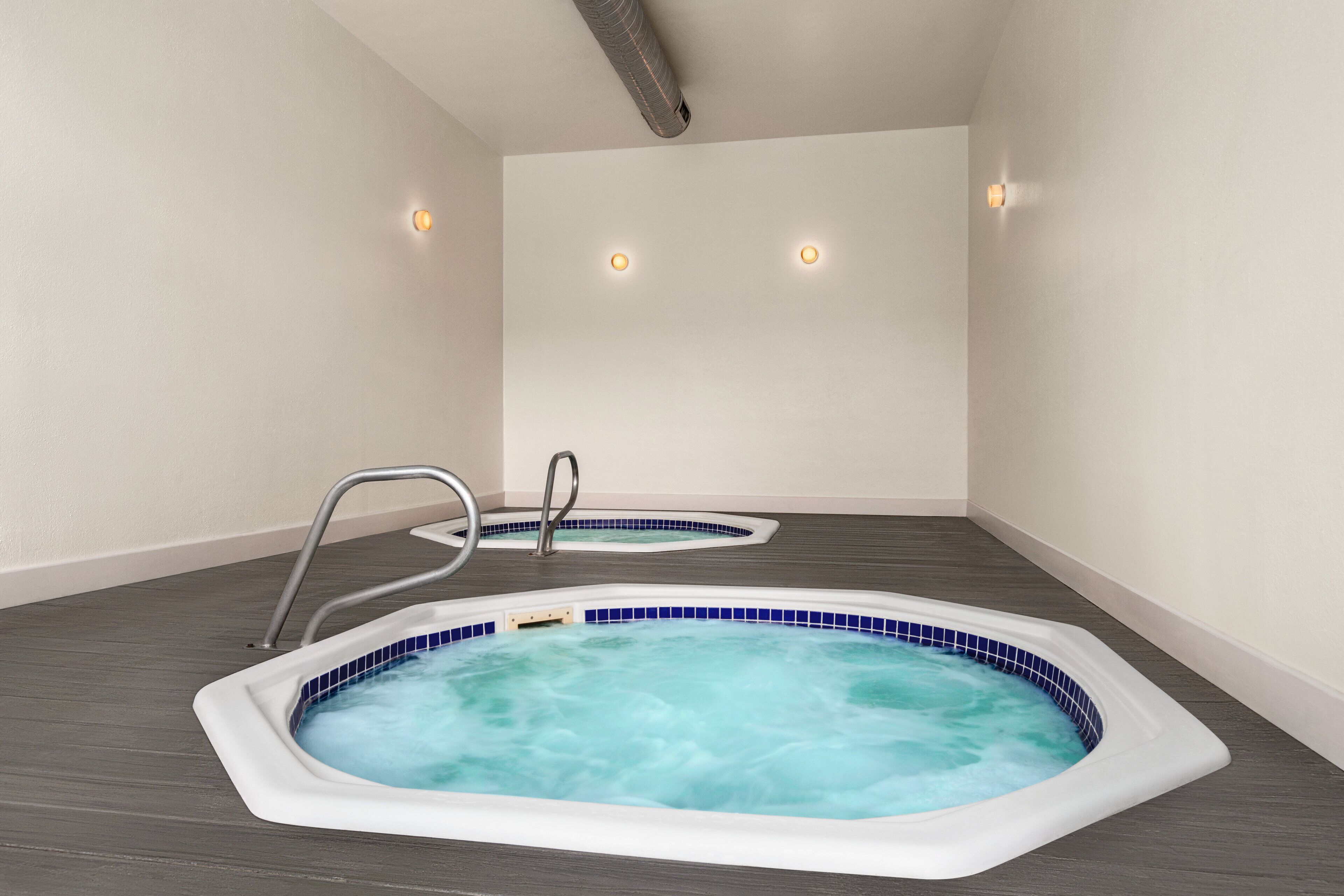 Een wellnessruimte met twee whirlpools, een metalen ladder en een ventilatieopening in het plafond.