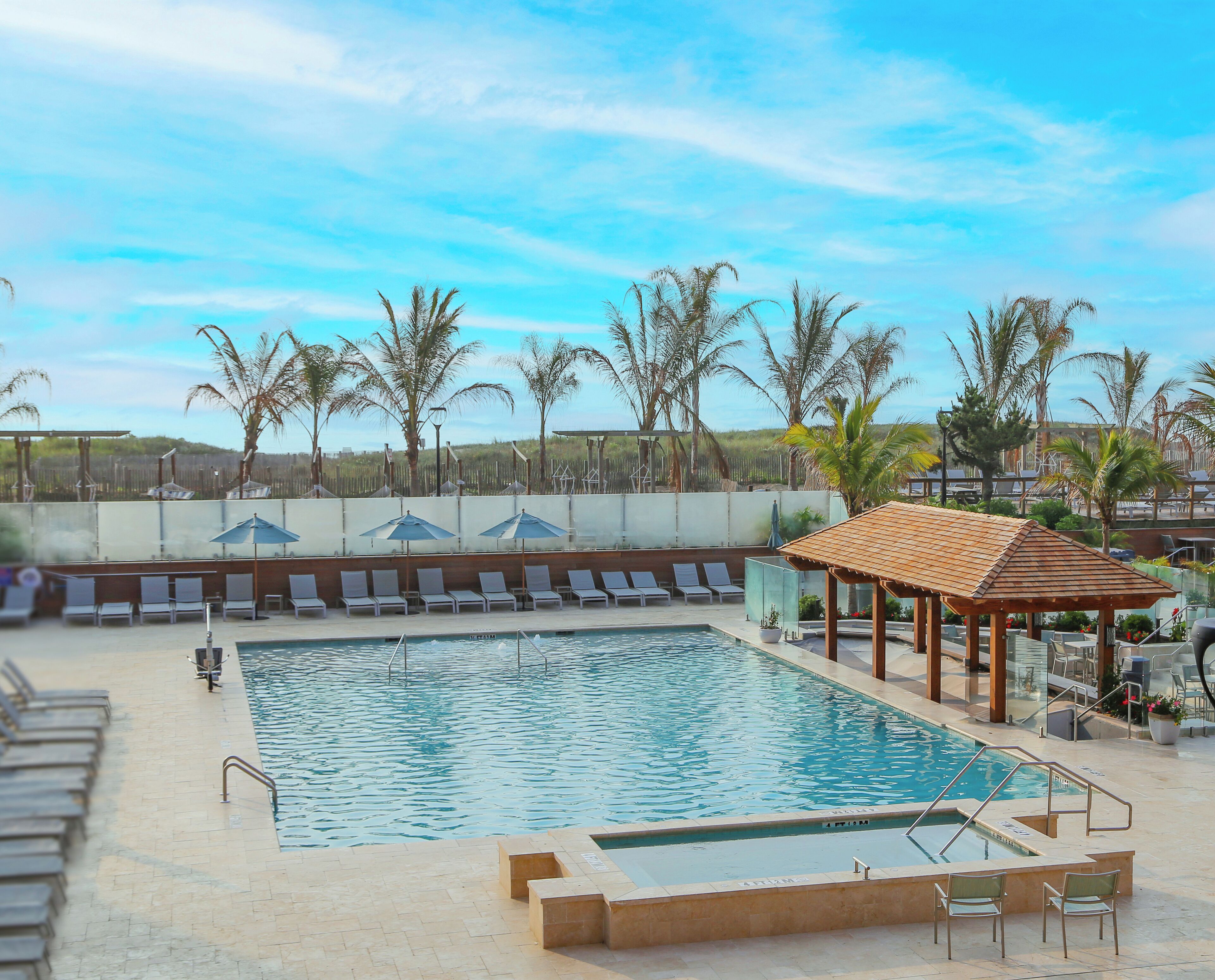 Une piscine entourée de palmiers, avec des chaises longues et des parasols.