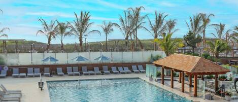 Una piscina con sillas de descanso y sombrillas, rodeada de palmeras.