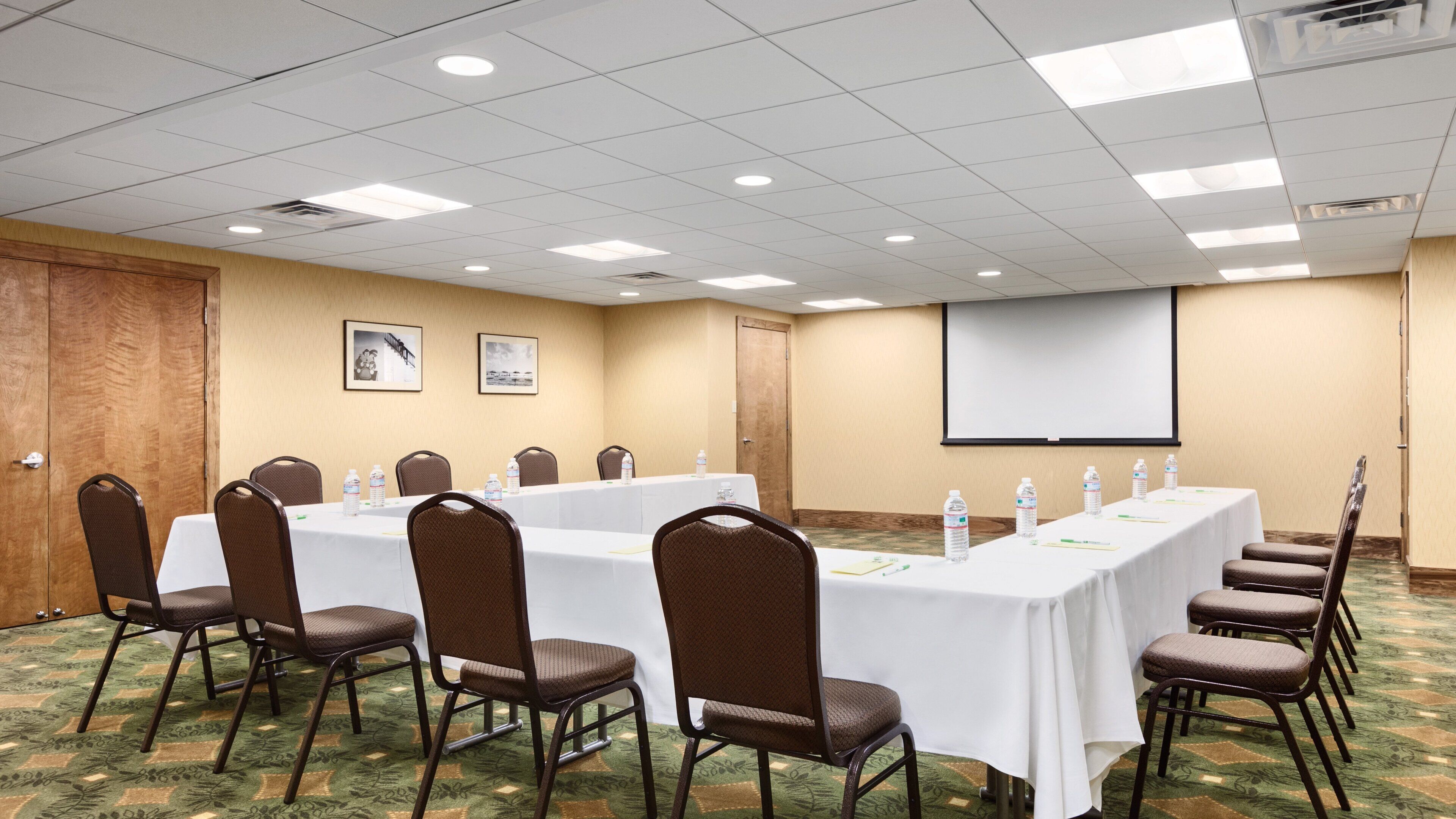 A conference room with a long table, chairs, a projector screen, and a carpeted floor.