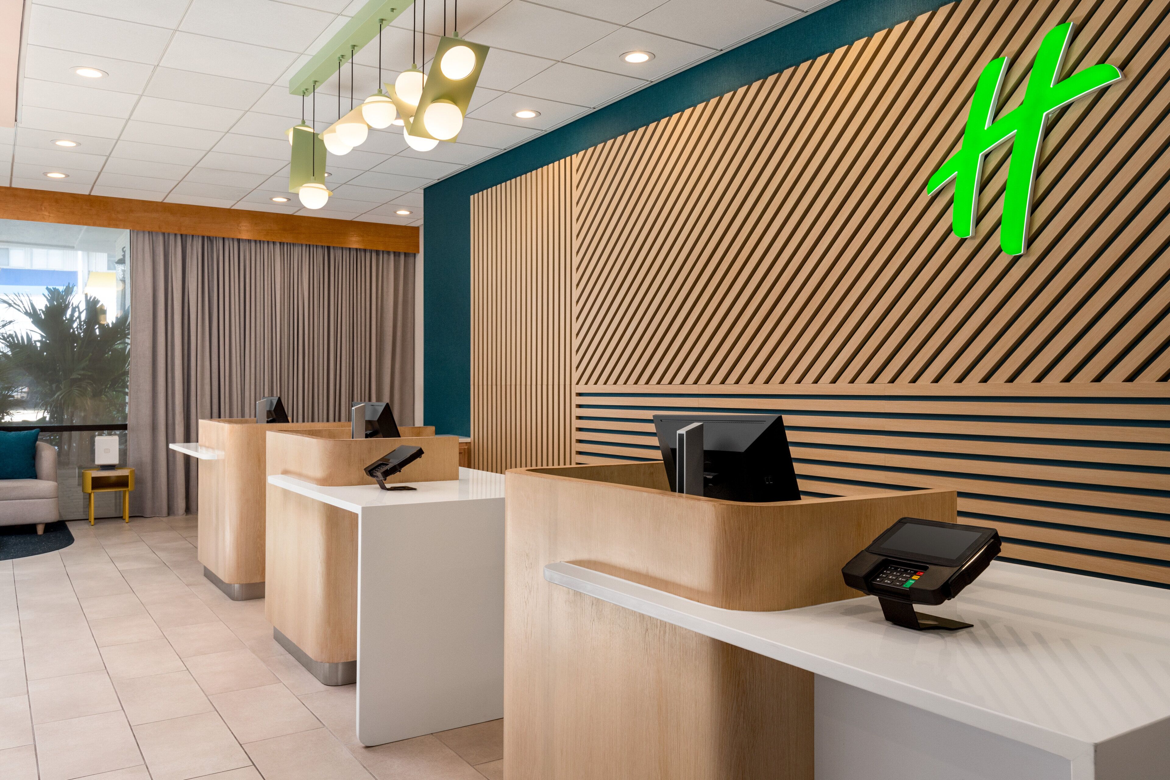 A reception area with a modern design, featuring a wooden reception desk, a green logo on the wall, and a ceiling with recessed lighting.