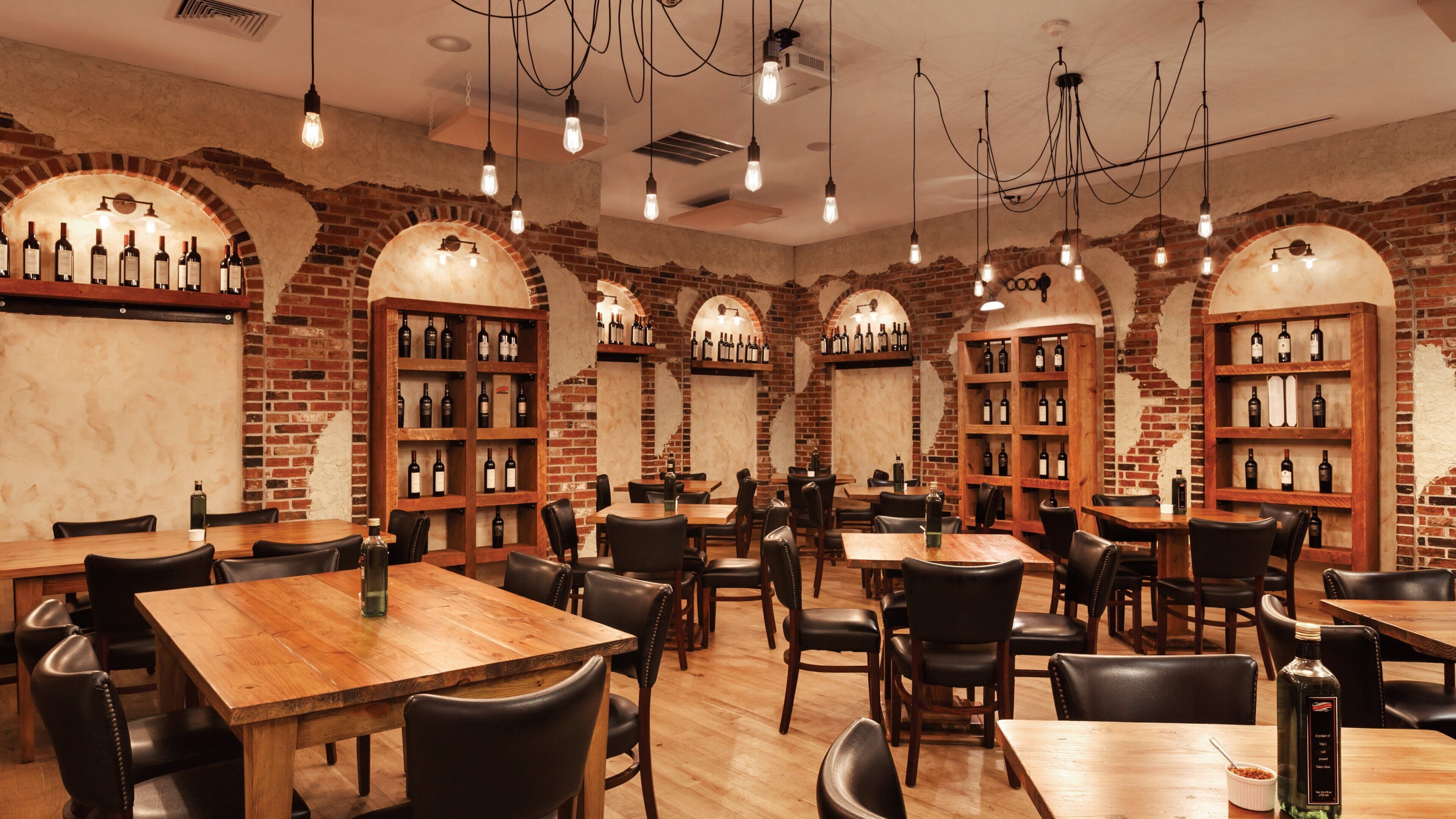A restaurant interior with brick walls, wooden tables, and shelves of wine bottles.