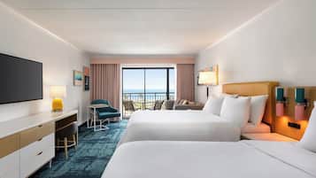 Habitación de hotel con dos camas, un escritorio, una silla, televisión y balcón con vistas.