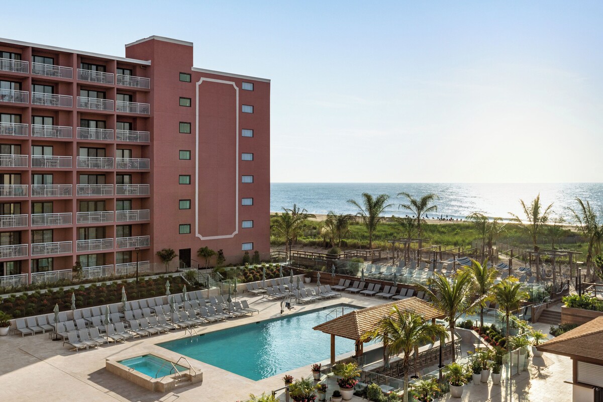 A hotel with a pool, lounge chairs, and a view of the ocean.