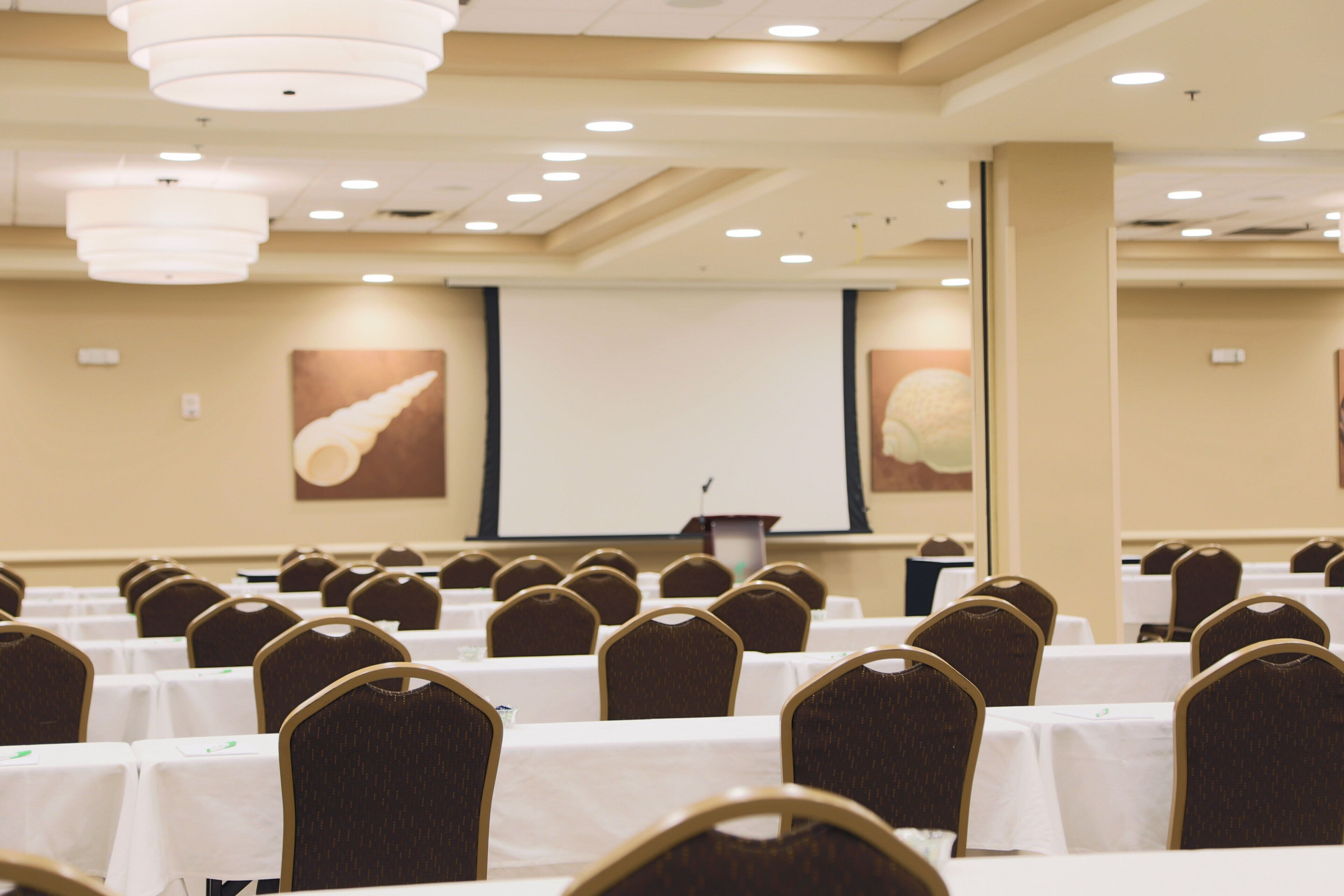 A conference room with rows of tables and chairs, a projector screen, and a podium.