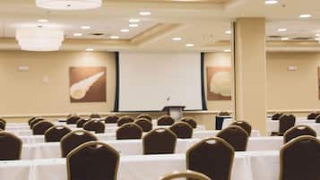 A conference room with rows of tables and chairs, a projector screen, and a podium.