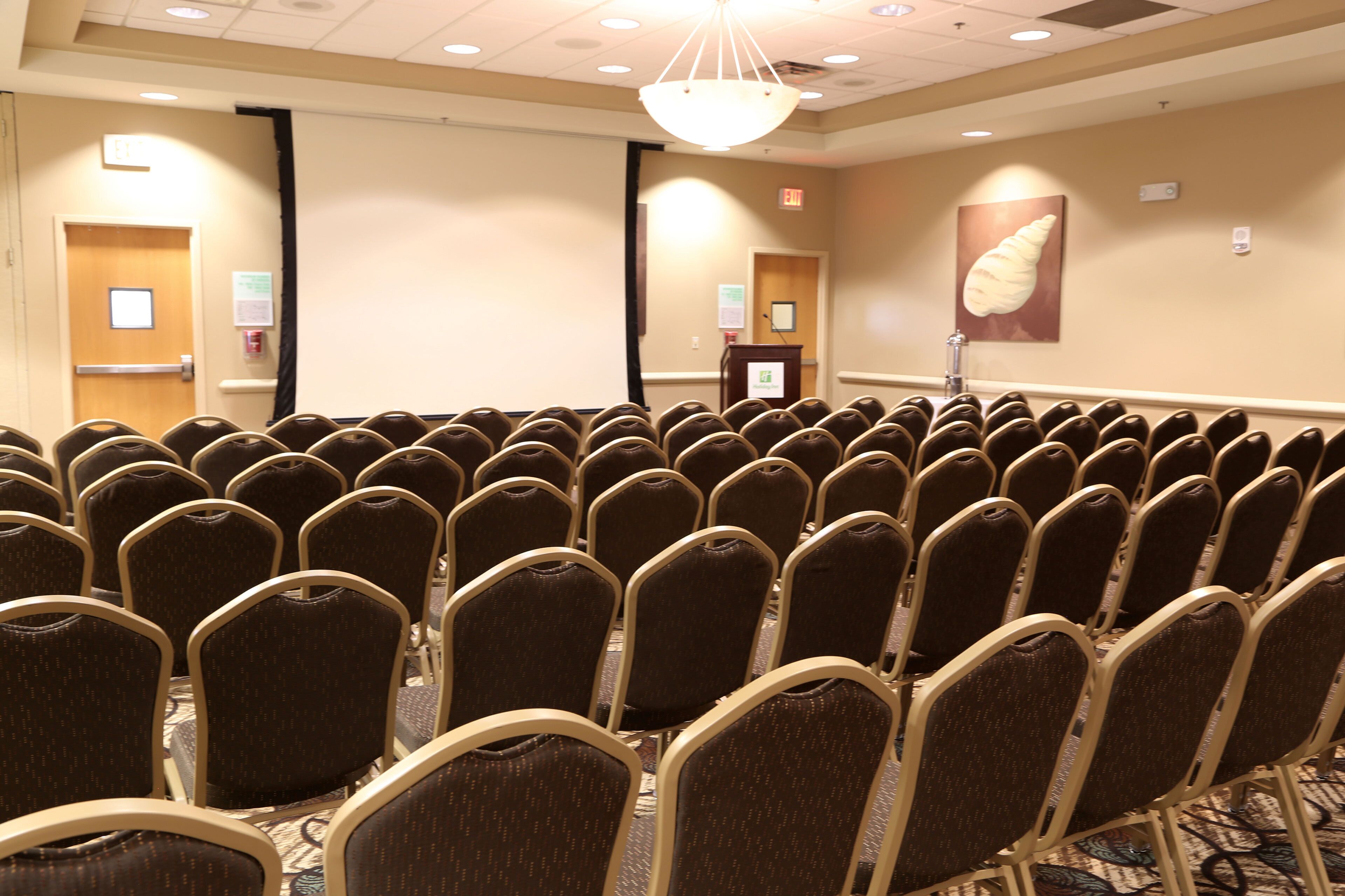 A conference room with rows of chairs, a podium, and exit signs.