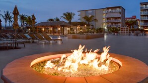 A fire pit in the center of a courtyard with lounge chairs and umbrellas in the background. - Holiday Inn Ocean City by IHG (Ocean City)