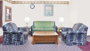 Ein Zimmer mit einem grünen Sofa, zwei gemusterten Sesseln, einem Holztisch, einer Uhr und einem gerahmten Bild an der Wand.
