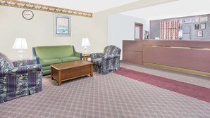 Eine Hotelhalle mit einem grünen Sofa, gemusterten Sesseln, einem Holztisch, einer Rezeption und einer Wanduhr.
