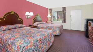 Ein Hotelzimmer mit zwei Betten, einem Schreibtisch, einem Stuhl, einer Lampe und einem Fernseher.