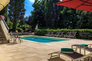 Área de piscina com espreguiçadeiras, escadas e um guarda-sol vermelho.