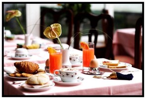 Una colazione con croissant, pasticcini, una tazza di caffè e succo d'arancia su un tavolo con tovaglia rosa.