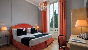 Une chambre d’hôtel avec un grand lit, deux lampes de chevet, un bureau avec une lampe et une vue sur l’extérieur par une fenêtre avec des rideaux.