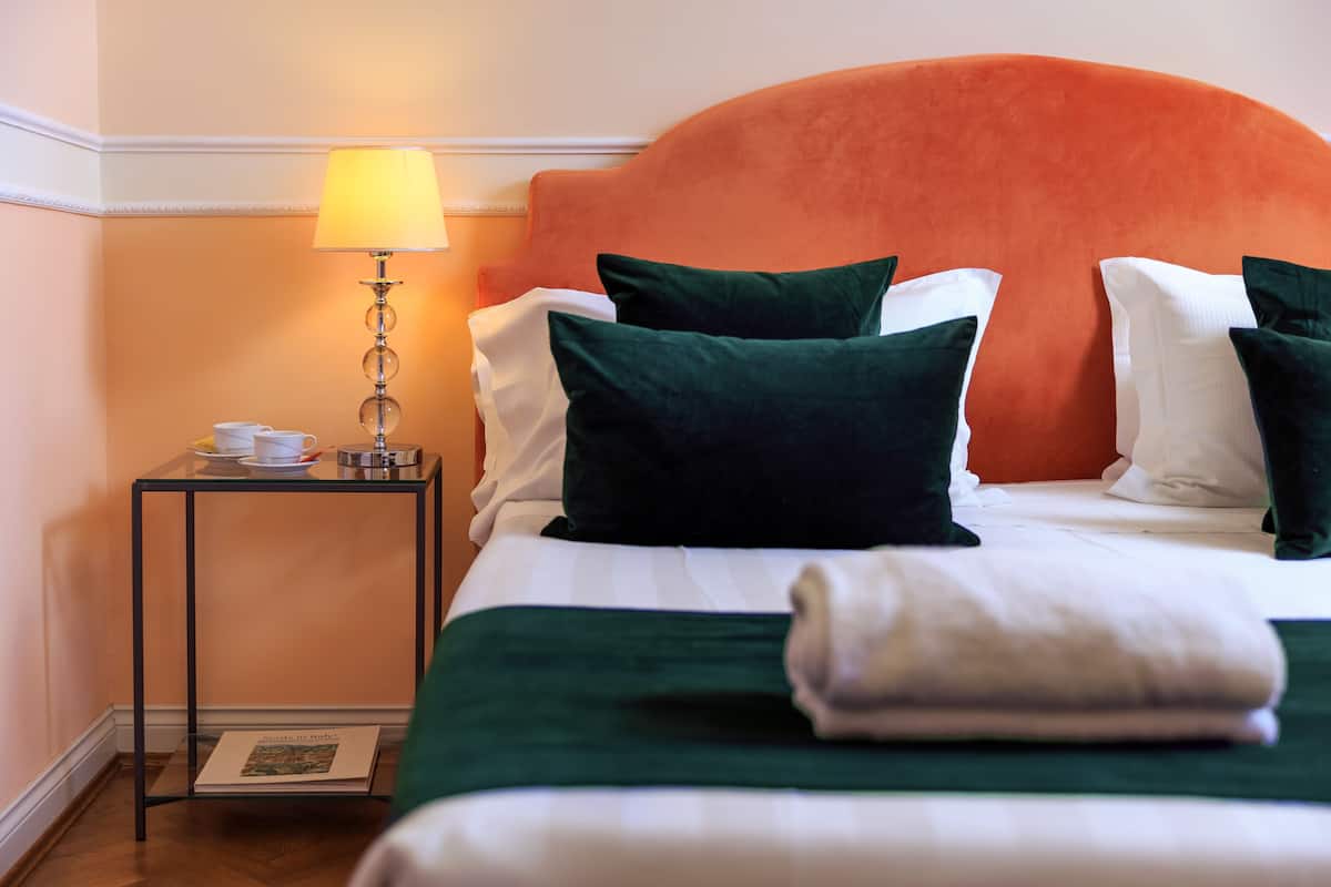 A neatly made bed with green and white bedding, a small bedside table with a lamp, and a framed picture on the floor.