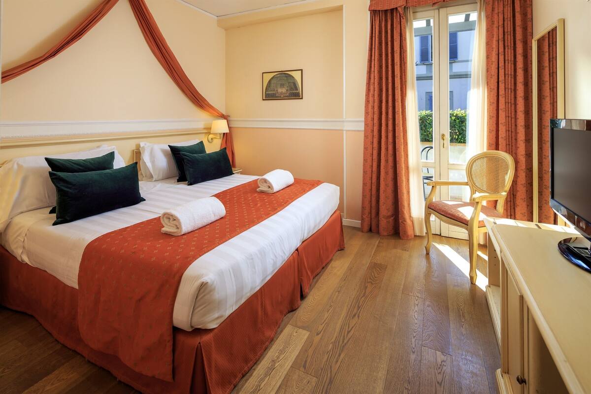 A hotel room with a large bed, two pillows, a TV, a chair, and a window with curtains.