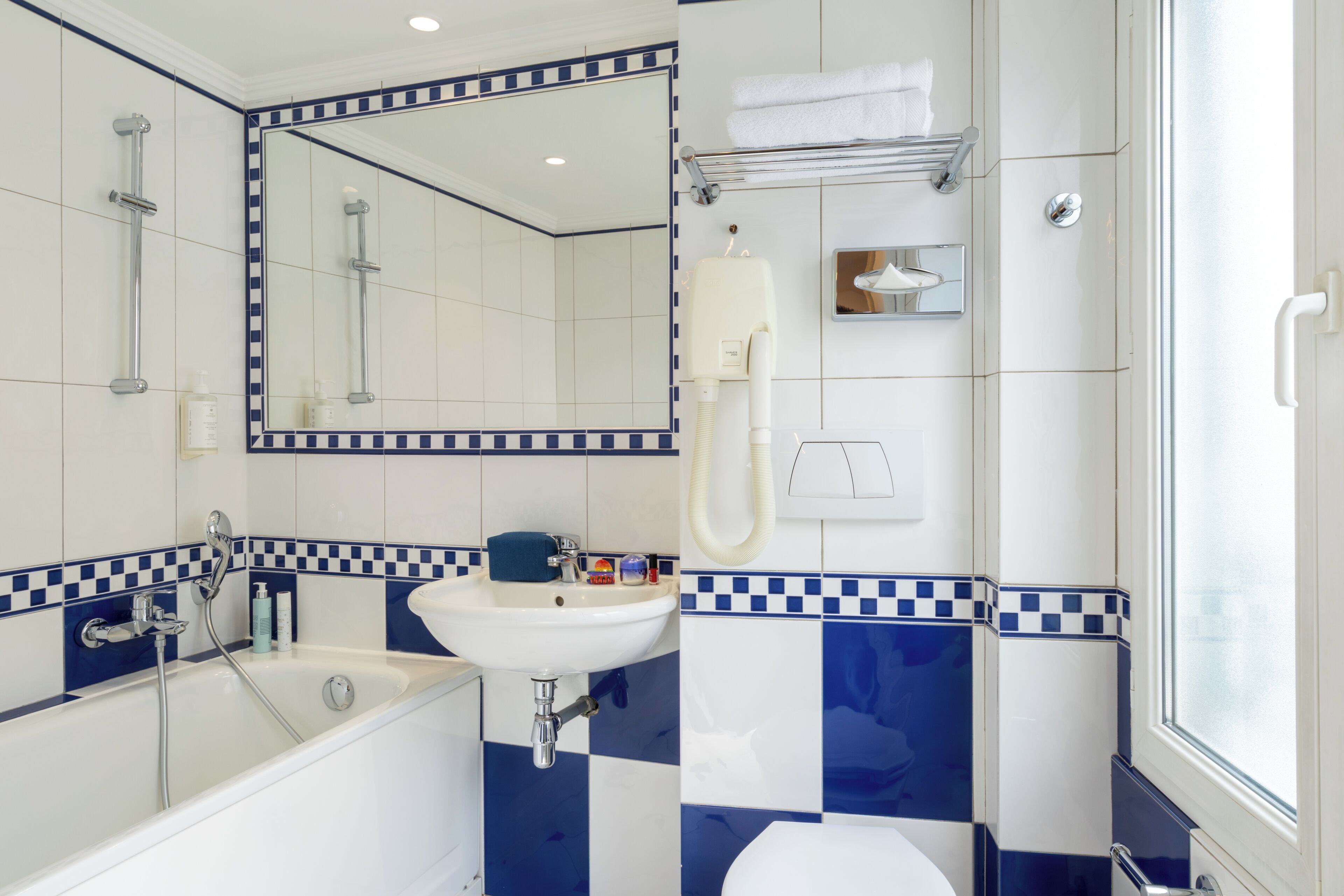 Un baño con bañera, lavabo e inodoro. Hay un espejo sobre el lavabo y una zona de ducha con puerta de cristal.