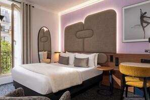 Habitación de hotel con una cama grande, una mesa redonda, una silla, un espejo y vista a la ciudad.
