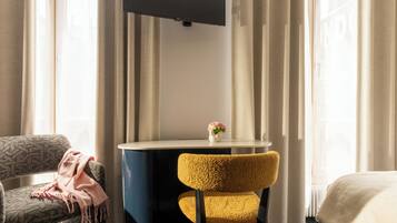 Una habitación de hotel con cama, escritorio y silla, y televisor en la pared.
