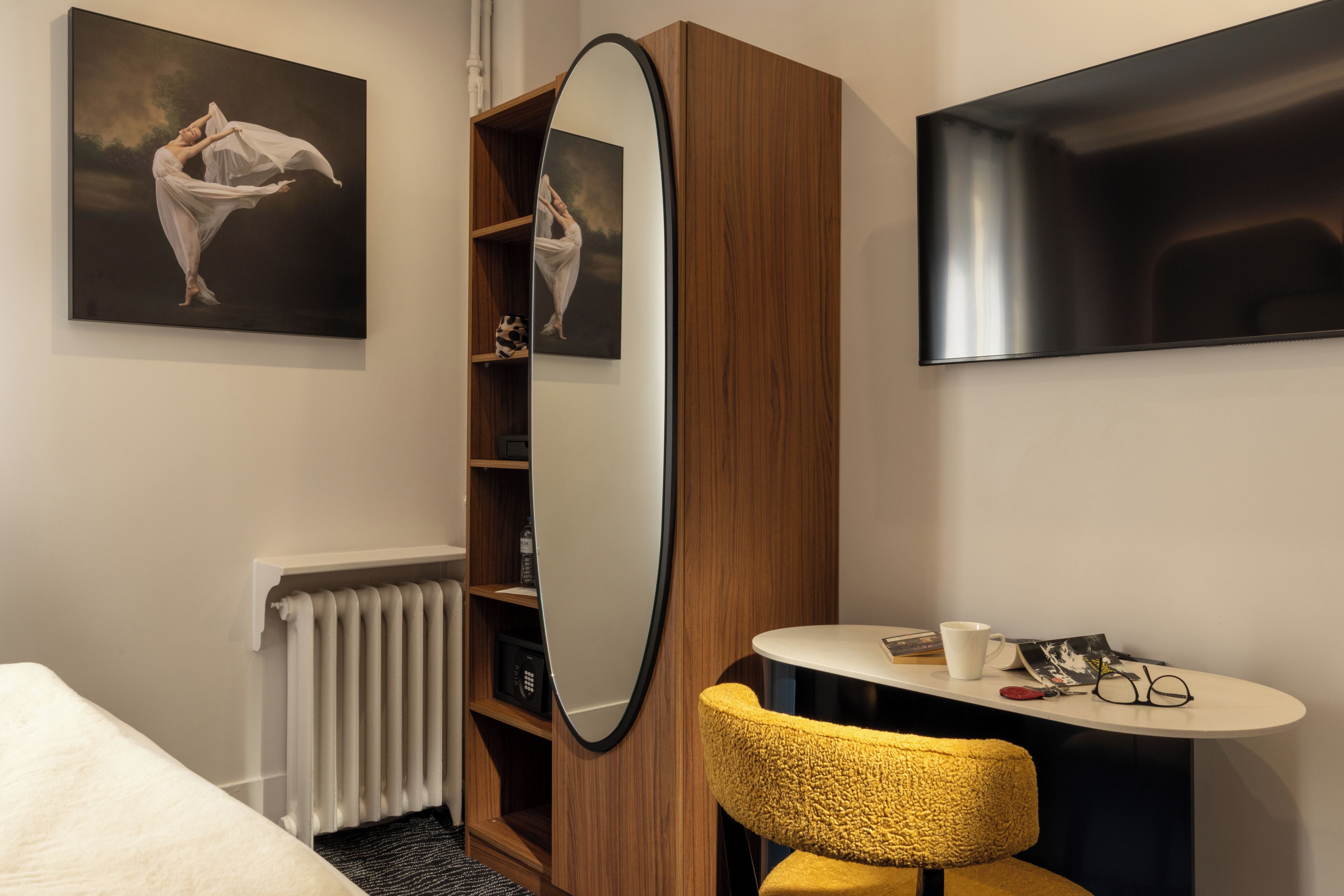 A hotel room with a bed, a round table with a chair, a large mirror, and artwork on the walls.