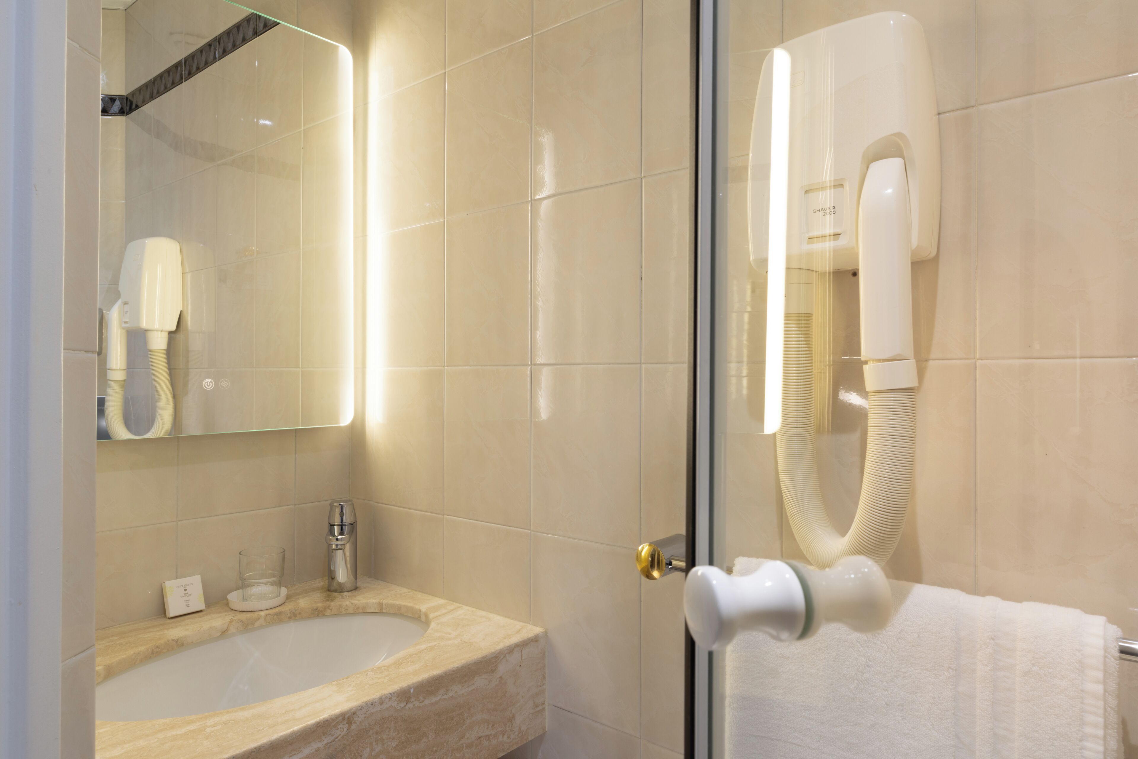 A bathroom with a glass-enclosed shower, a sink with a marble countertop, and a towel rack with a white towel.