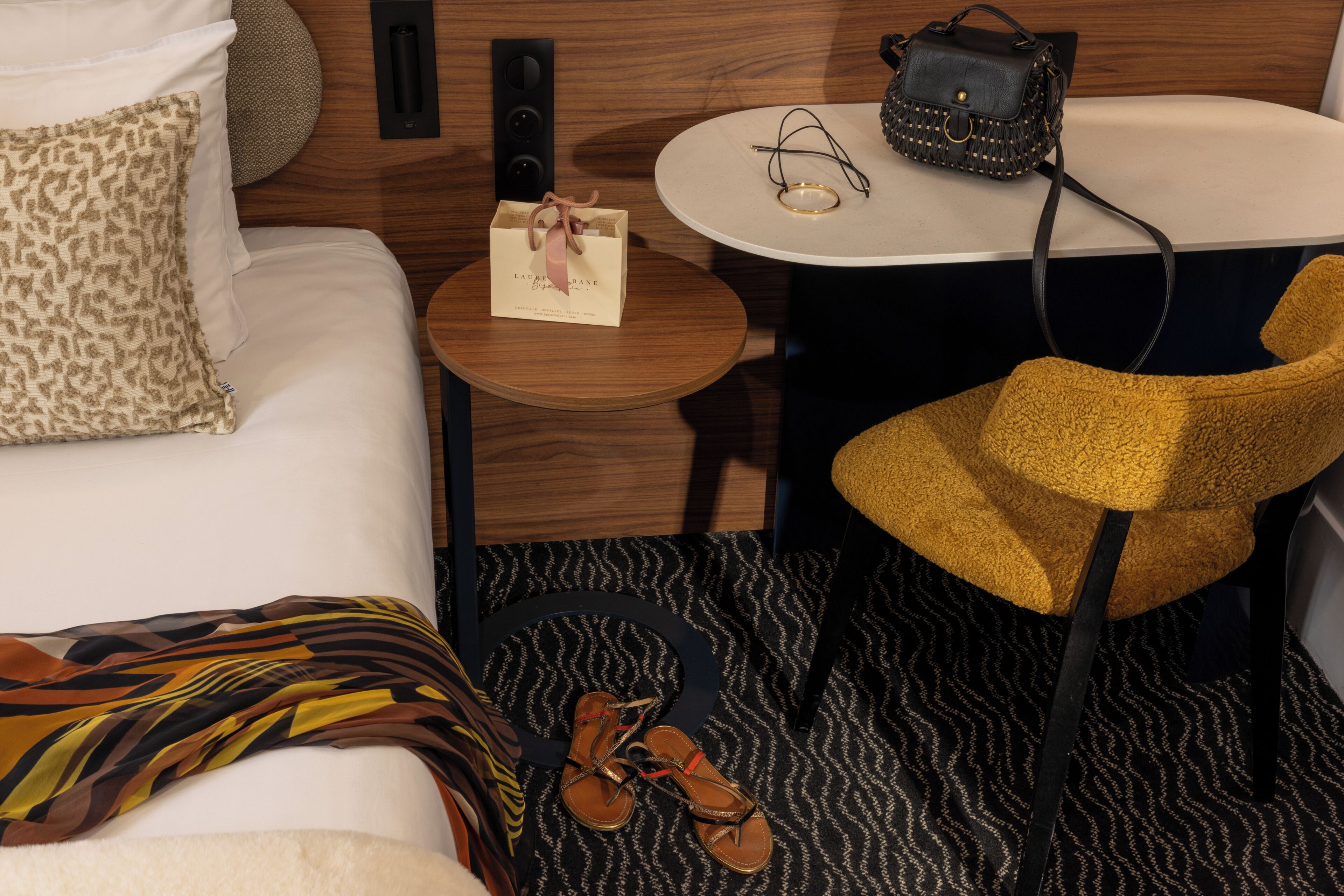 Une chambre d’hôtel bien rangée, avec un lit, une petite table ronde, une chaise, une paire de chaussures et un sac à main.