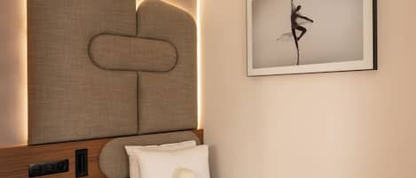 A bedroom with a headboard, a bed with pillows, a teddy bear, and a framed picture on the wall.