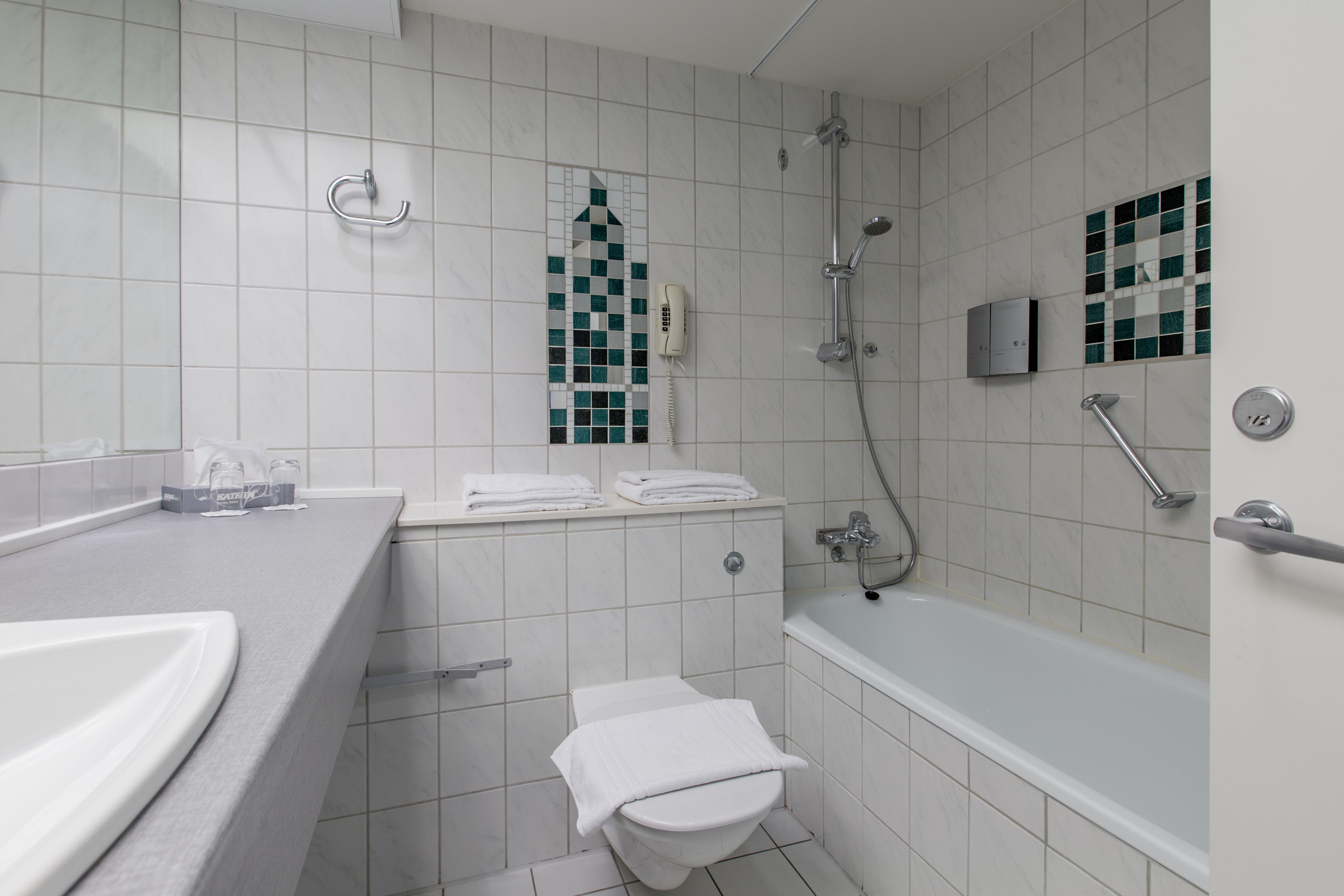 A modern bathroom with a white sink, toilet, and bathtub. There is a towel rack above the sink and a showerhead above the bathtub.