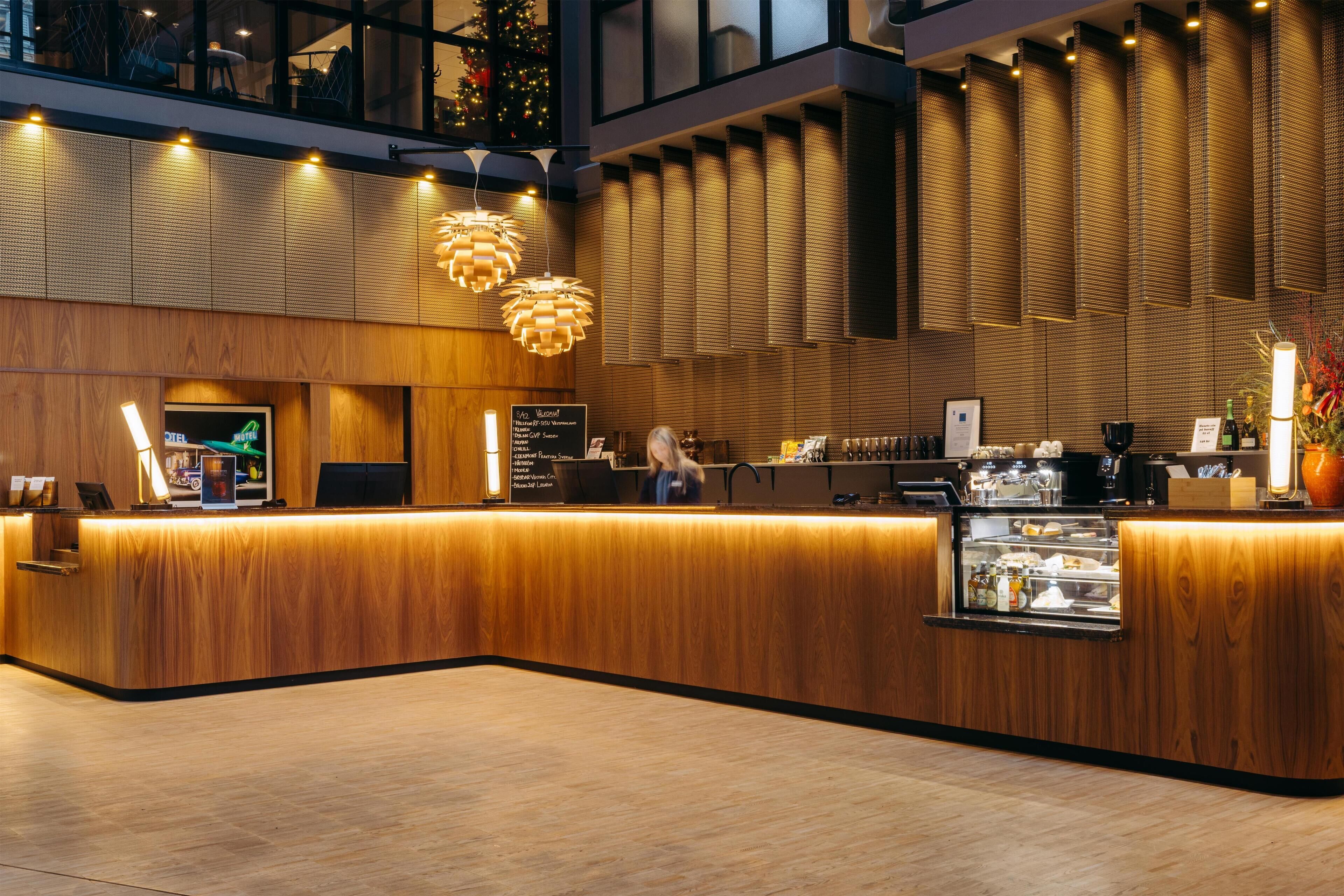 A modern hotel reception area with a wooden reception desk, a digital screen, and a glass display case.