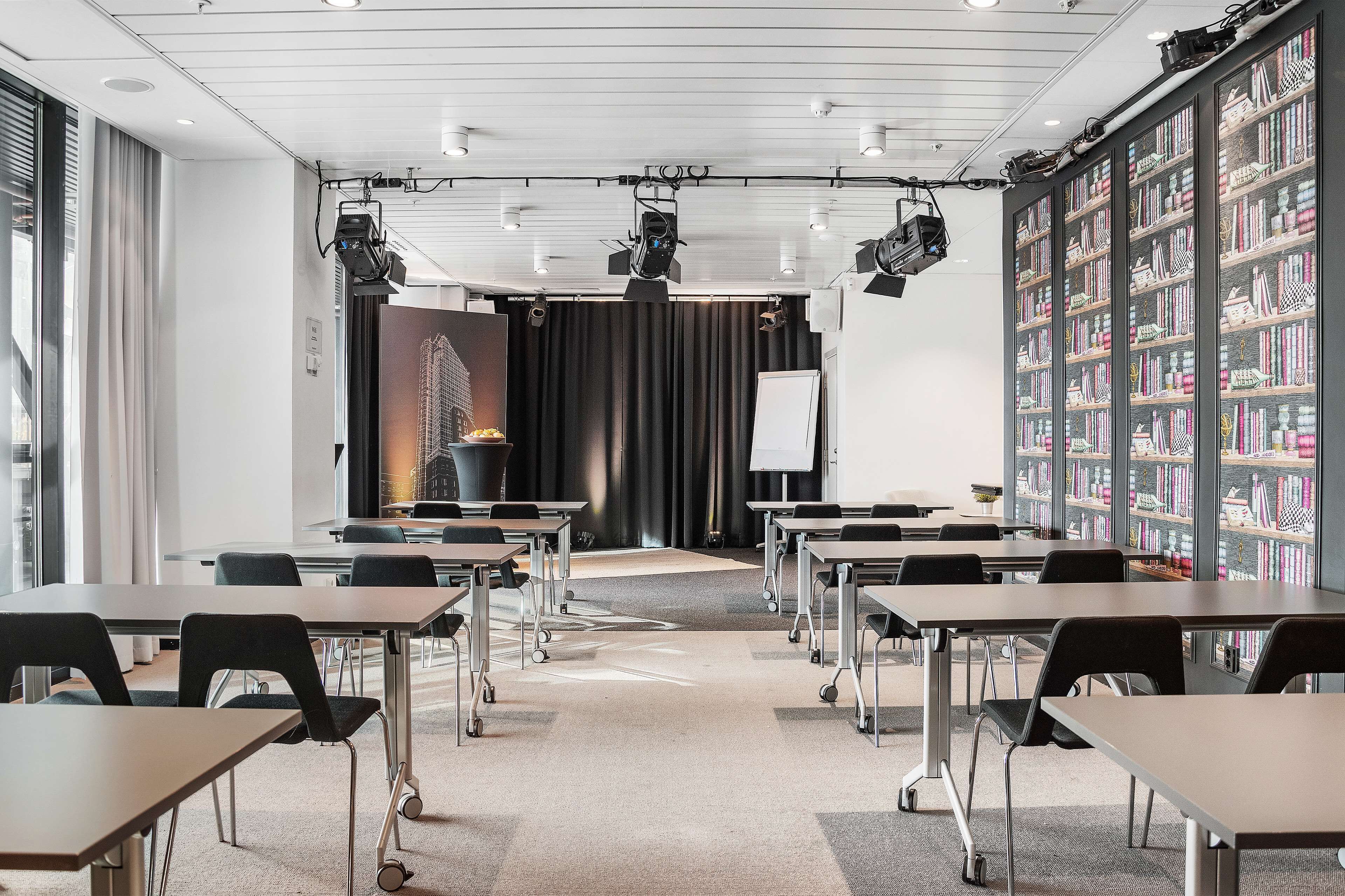 Une salle de conférence équipée de tables, de chaises, d’un projecteur et d’une bibliothèque.