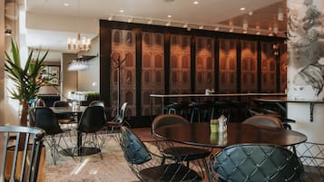 A modern dining area with round tables and black wireframe chairs, a large potted plant, and a decorative wall with a floral pattern.