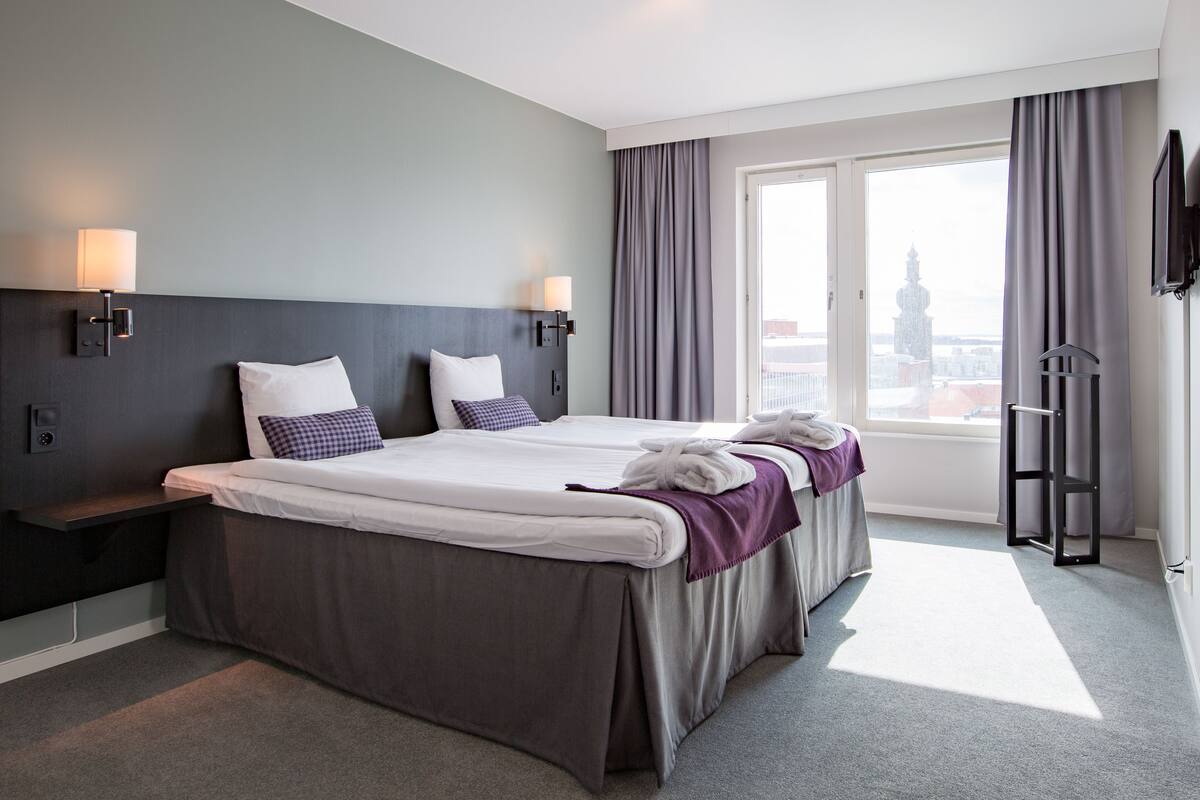A hotel room with two beds, a large window, and a city view.