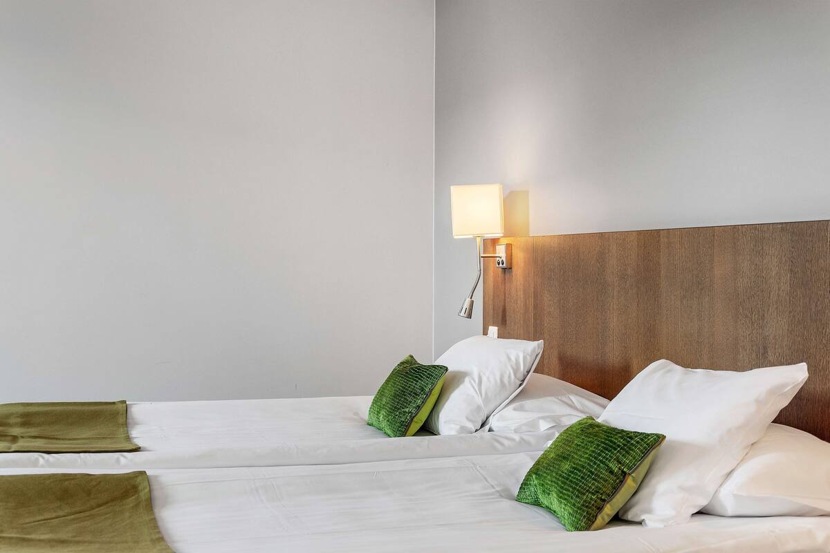 A hotel room with two beds, a nightstand with a lamp, and a wooden headboard.
