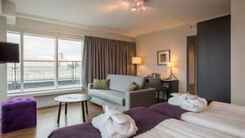 A hotel room with a bed, a sofa, a small table, a TV, and a window with curtains.