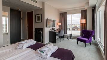 A hotel room with a bed, a desk, a chair, a TV, and a view of the city.