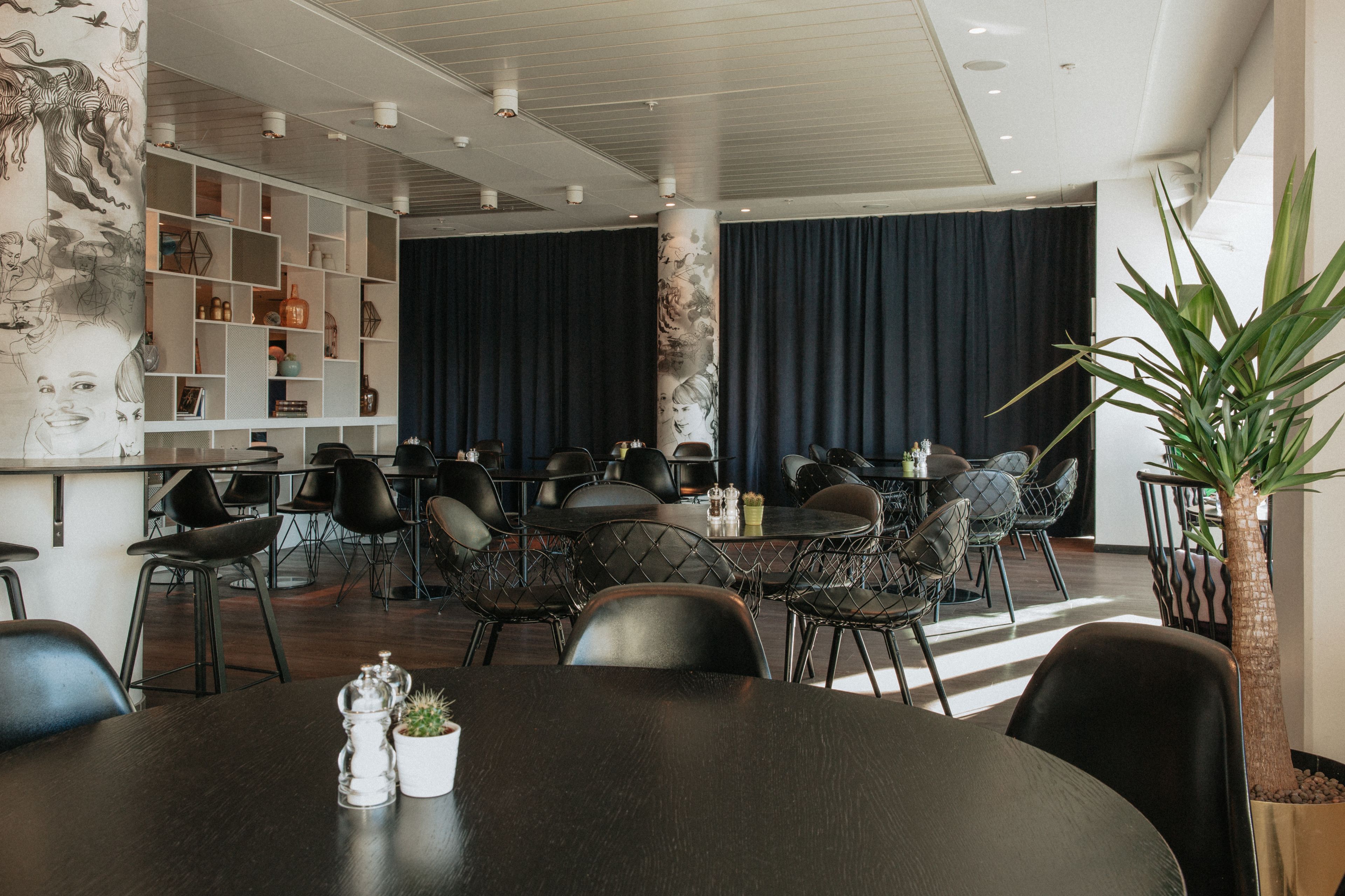 Un comedor moderno con sillas negras, una mesa redonda y una pared decorativa con estantes.