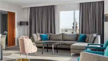 Una sala de estar moderna con un sofá gris, sillas verde azulado, una mesa de centro redonda y un ventanal con cortinas.