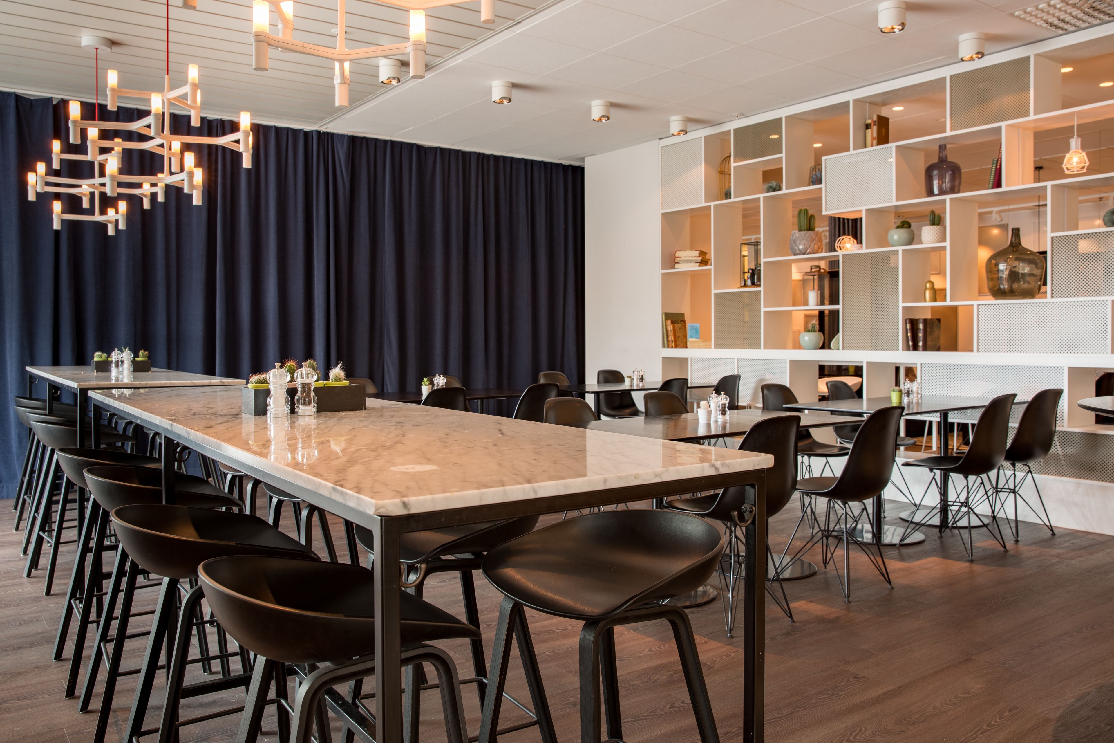 A modern conference room with a long table, black chairs, and a white shelving unit with decorative items.