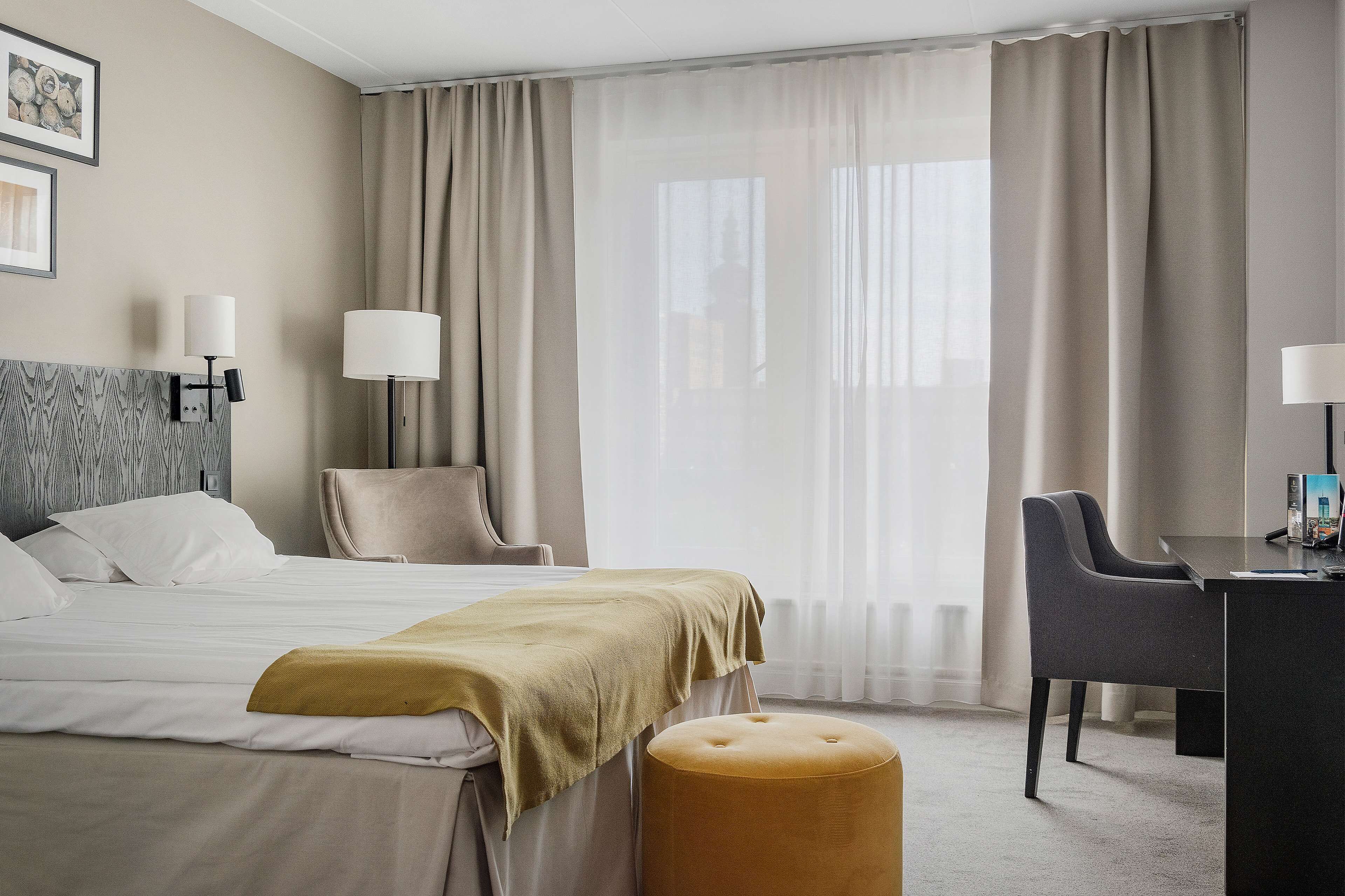 Una habitación de hotel con cama, dos sillas, un escritorio y un ventanal con cortinas.