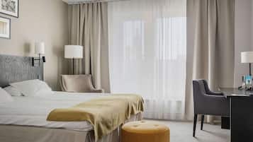 Una habitación de hotel con cama, dos sillas, un escritorio y un ventanal con cortinas.