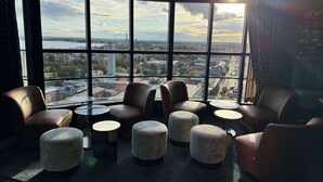 Un espace de détente moderne avec des fauteuils et des poufs en cuir, de grandes fenêtres offrant une vue sur la ville et une petite table.