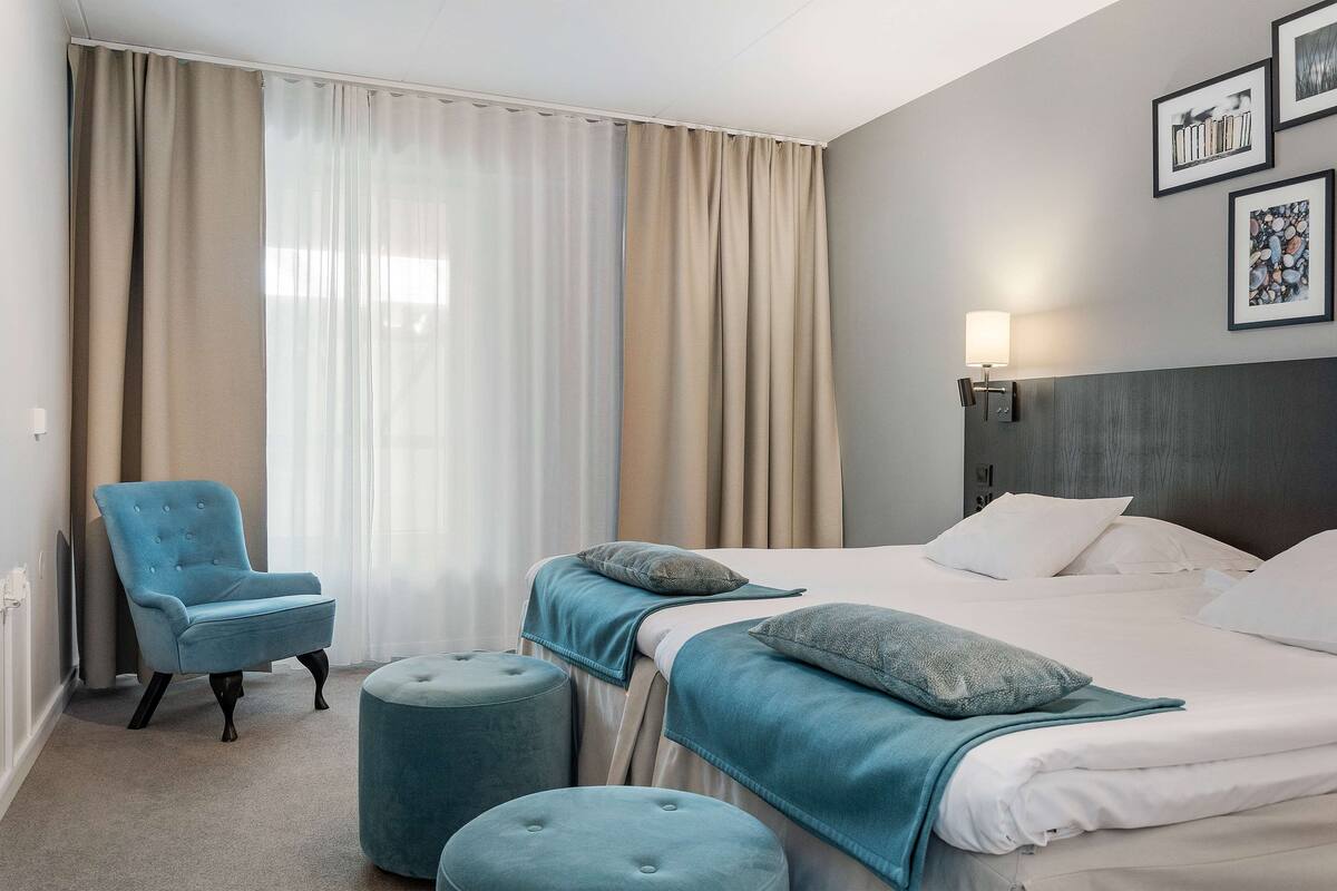 A hotel room with a bed, two ottomans, a chair, and a lamp.