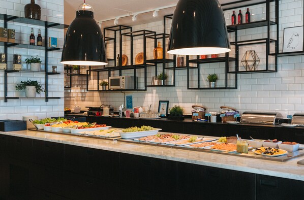 Un bufé con diversos alimentos y una cocina moderna con estantes negros y azulejos blancos.