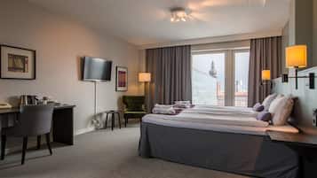 A hotel room with a bed, desk, chair, TV, and large windows with curtains.