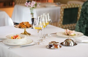 Una mesa de comedor dispuesta con un bol de fruta, croissants, copas de vino y condimentos.