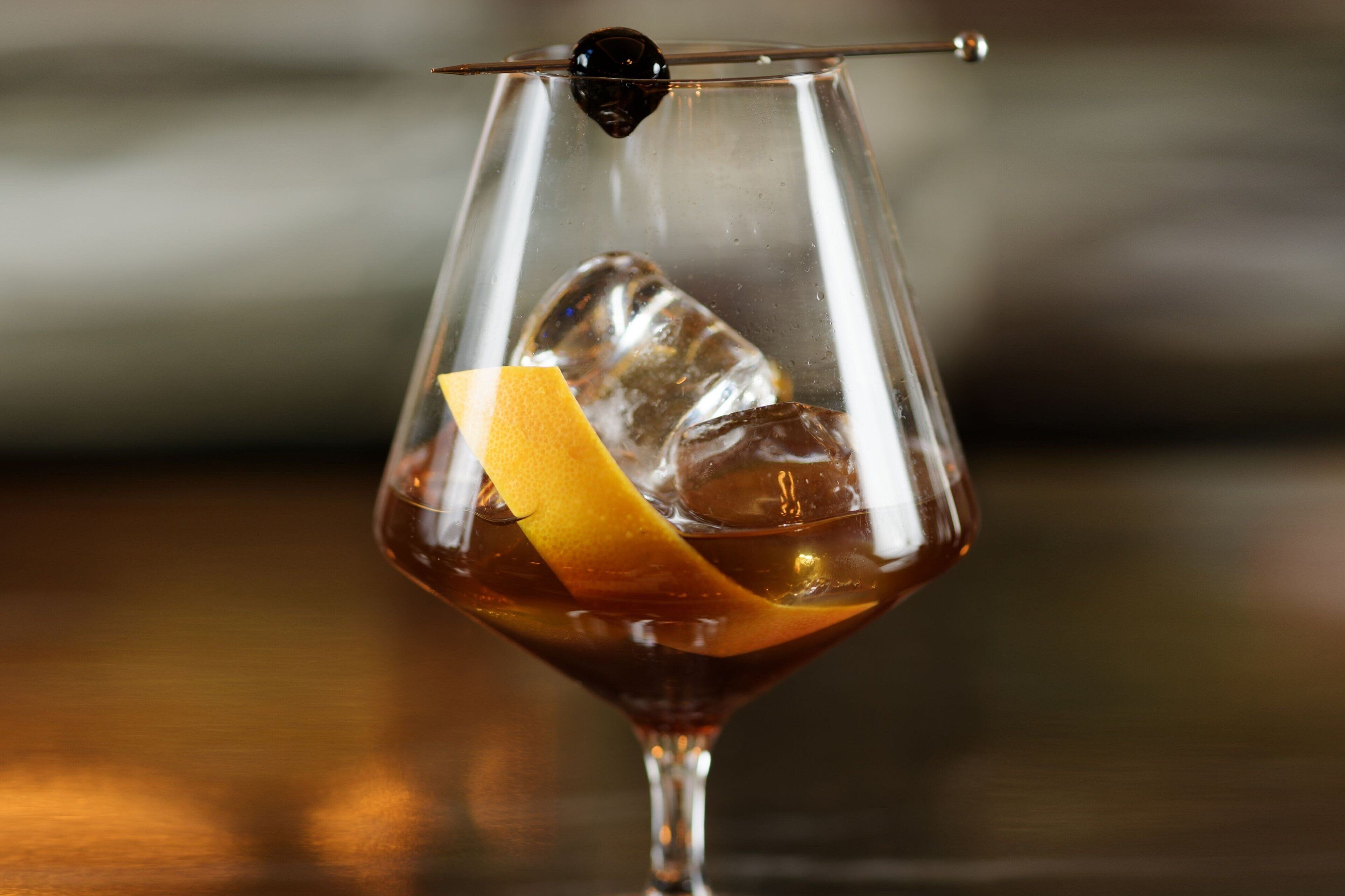 Un verre transparent rempli de glaçons et garni d’une tranche de zeste d’orange.
