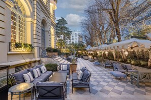 Un patio al aire libre con piso de cuadros, arreglos de asientos y vistas a un edificio con ventanas grandes y un balcón.