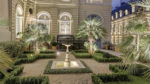 Um edifício imponente com uma fonte, rodeado por jardins bem cuidados e palmeiras.